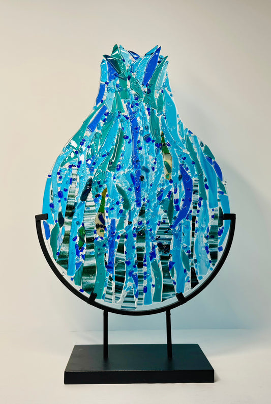 Decorative abstract glass sculpture to represent a teardrop or raindrop water design of various blues in a black metal stand.